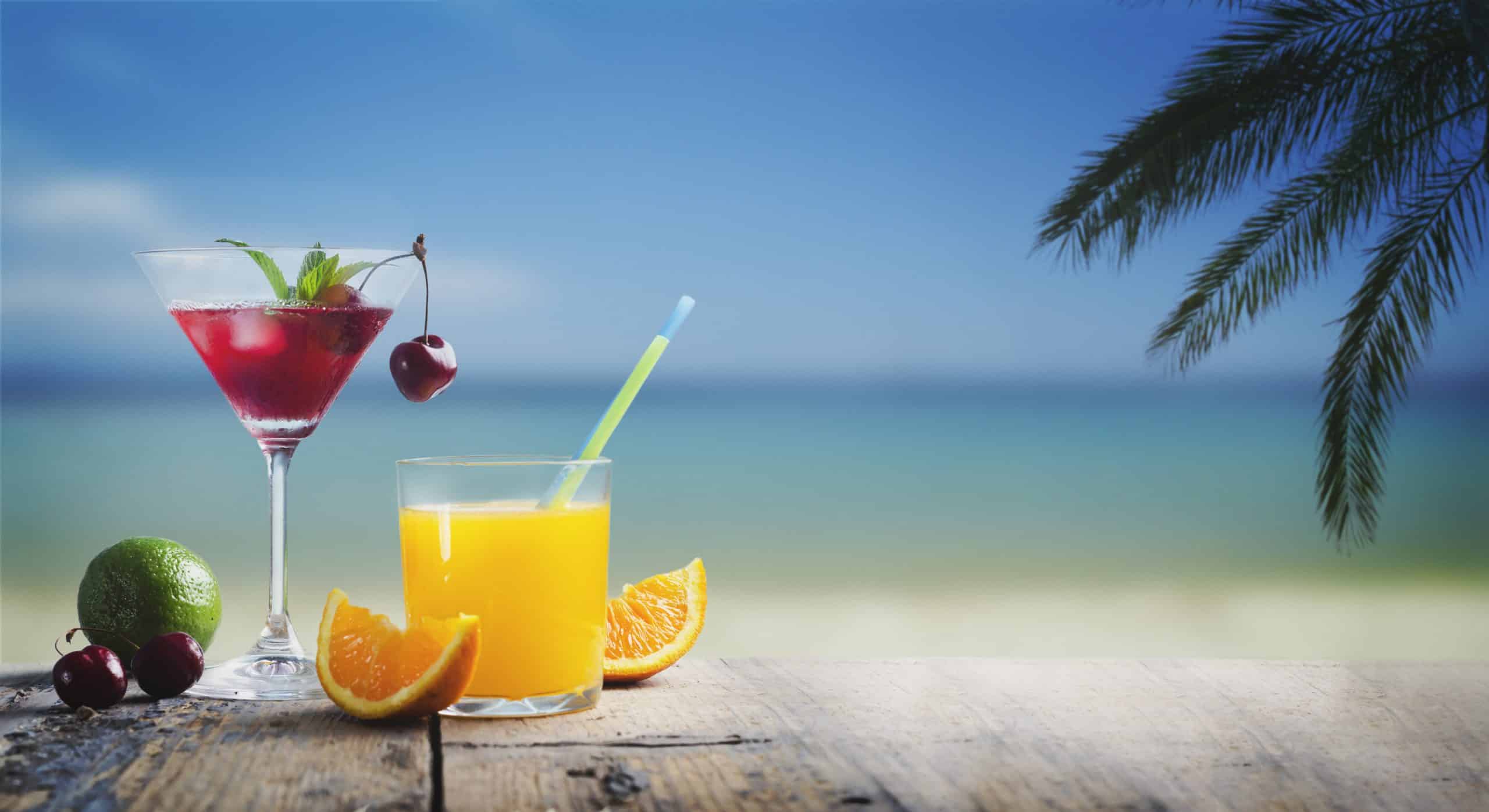 Cherry cocktail in martini glass and orange juice vodka on tropical sandy beach.